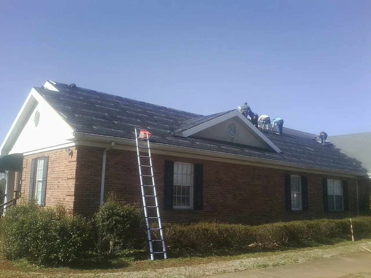 Crew tearing shingles off a brick ranch roof with a ladder set — Metal Roof Repair work by our crew in Boonville
