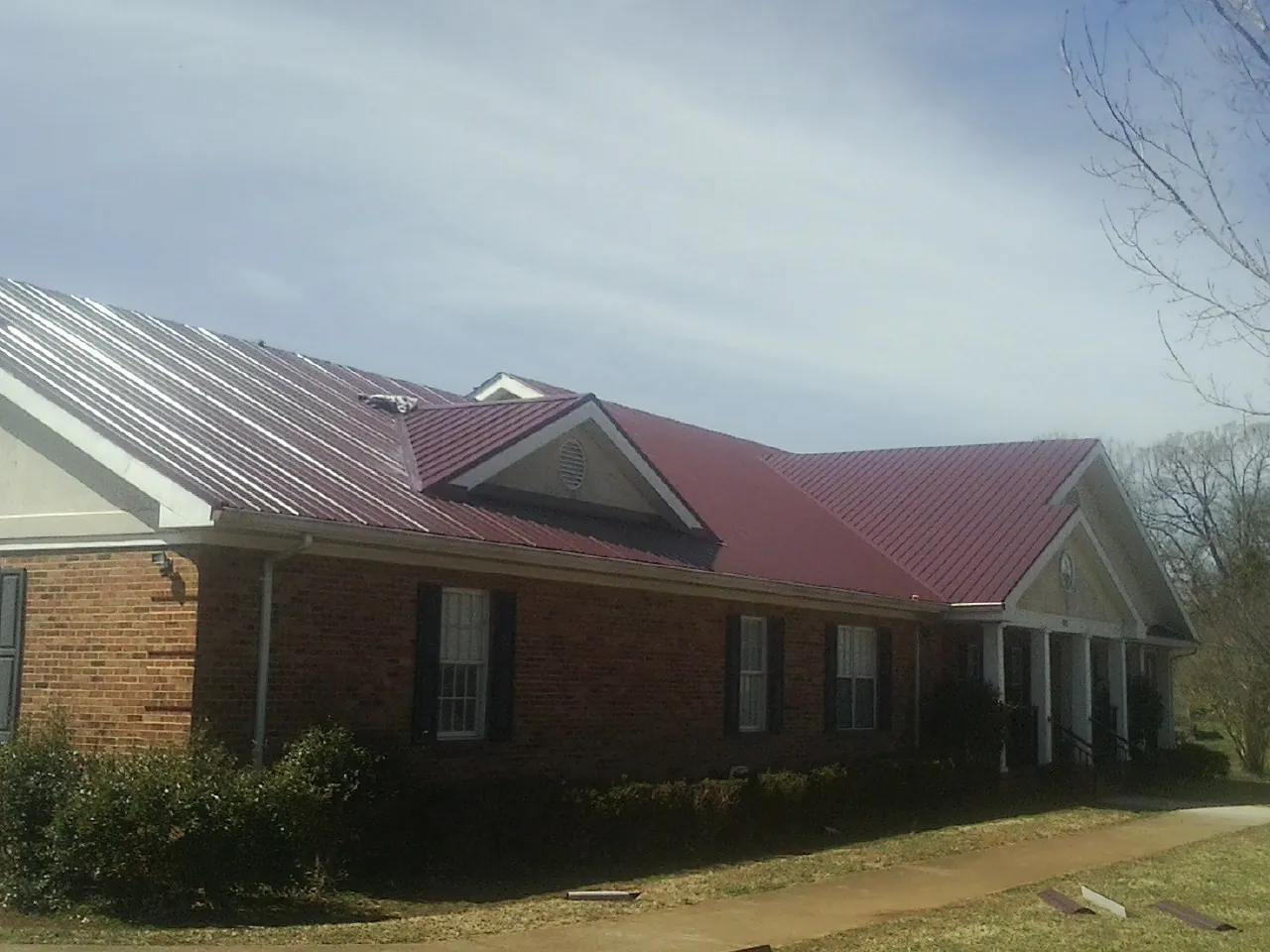 Red metal roof with gabled entries on a long brick building, from a Hail Damage Roof Repair job in Boonville