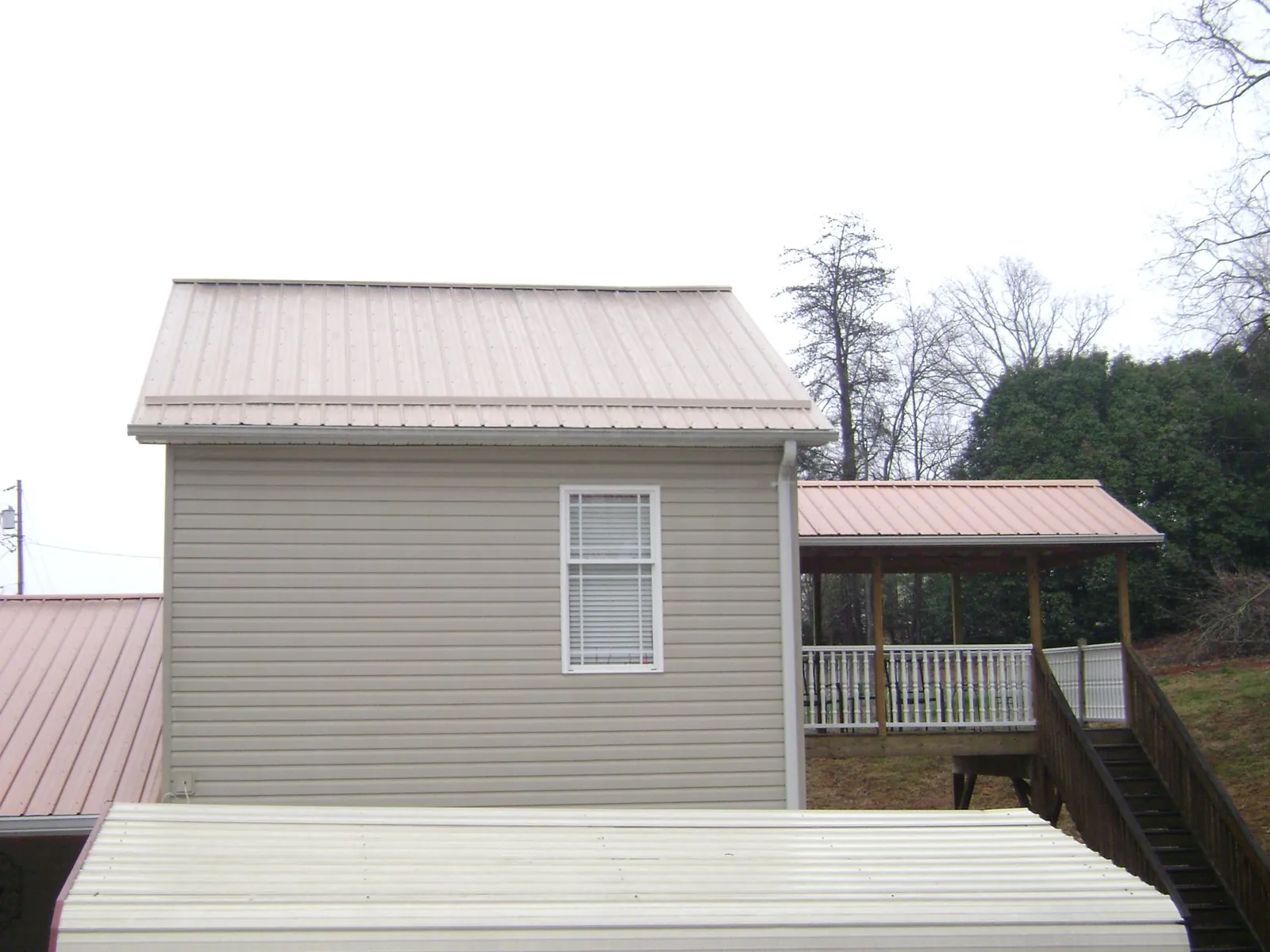 Tan metal roofs on a two story addition and attached porch, from a Roof Replacement job in Boonville